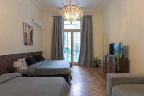 Ein Hotelzimmer mit zwei Betten, einem Chandelier, einem Fernseher und Blick durch ein Fenster.