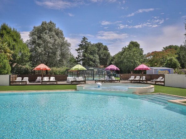 A swimming pool with lounge chairs and umbrellas, surrounded by trees and a clear sky. - Comfortable mobile home - 2 guests (Les Achards)