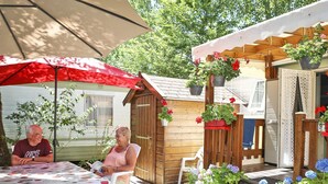 An outdoor patio with a table, chairs, a wooden shed, and hanging flower pots. - Comfortable mobile home - 2 guests (Les Achards)