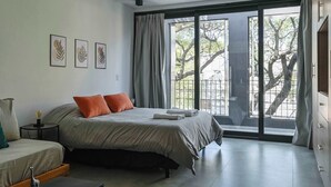 Ein Schlafzimmer mit einem Bett, einem Nachttisch, einer Lampe und einem Fenster mit Vorhängen.