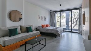 Ein modernes Zimmer mit einer Schlafcouch, einem Bett, einem runden Spiegel und einem Fenster mit Vorhängen.