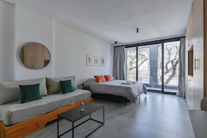 A modern room with a sofa, a bed, a round mirror, and a window with curtains. - MOT Rentals + Black Ravignani 2B - 3 pax Loft Palermo Hollywood (Buenos Aires)