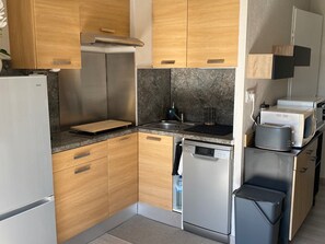 Eine kompakte Küche mit Holzausstattung, einem Edelstahlkühlschrank, einer Spülmaschine und einer Mikrowelle.