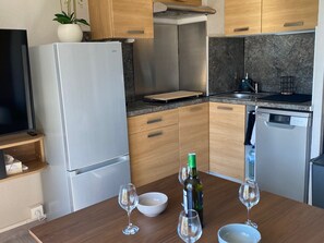 Eine moderne Küche mit Einbaukühlschrank, Geschirrspüler, Holzschränken und einem Esstisch, gedeckt mit Weingläsern und Schüsseln.