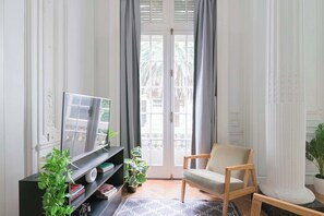 Ein Wohnzimmer mit Fernseher, einem Sessel, einem Bücherregal und einer Topfpflanze.