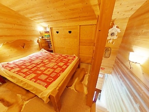 Ein Schlafzimmer in einer Holzhütte, mit einem Bett, einem Bücherregal und einer Wand mit einer herzförmigen Aussparung.