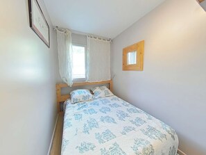 A bedroom with a bed, a window with curtains, a wooden headboard, and a small mirror on the wall. - Family apartment at the foot of the slopes - 7 guests (Le Grand-Bornand)