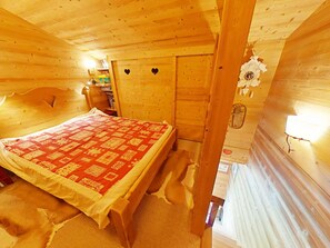 Quarto de cabana de madeira com cama, estante e parede com um recorte em formato de coração.