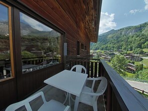 Varanda de madeira com mesa e cadeiras, com vista para uma aldeia montanhosa.
