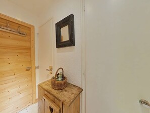 Eine Holztür mit Griff, ein kleines Holzschränkchen mit Korb und ein Spiegel an der Wand.