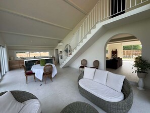 Un vaste espace de vie doté d’un haut plafond, d’un escalier, d’une table à manger avec des chaises, d’un canapé et d’une grande fenêtre.