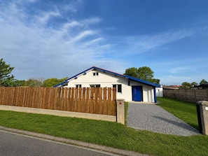 Ein eingeschossiges Haus mit blauem Dach, Holzzaun und Kiesweg.