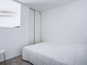 Ein Schlafzimmer mit Bett, Fenster, Klimaanlage und einer Schiebetür.