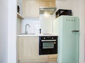 Eine kleine Küche mit Spüle, Mikrowelle, Kühlschrank und Einbauofen.