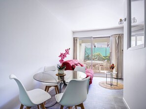 Ein modernes Wohnzimmer mit einem Glastisch, weißen Stühlen, einem roten Sofa und Blick auf einen Garten durch eine Schiebetür.