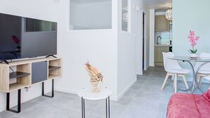 A modern living room with a flat-screen TV, a small round table, and a pink sofa. - Modern apartment, AC and parking - 3 guests (Canet-en-Roussillon)