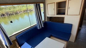 Interior compacto de una caravana con una zona de asientos tipo banco de color azul, una mesita y una ventana con vistas al agua.