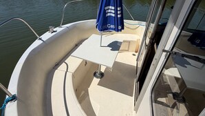Interior de un barco con una mesa, un paraguas azul y vistas al agua.