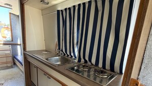 Una kitchenette compacta con un lavamanos de acero inoxidable, una estufa a gas y una cortina a rayas.