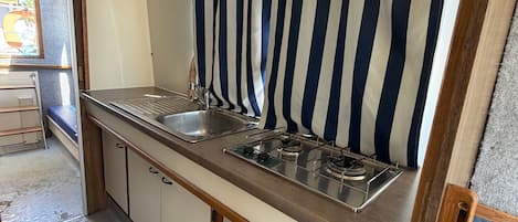 A compact kitchenette with a stainless steel sink, a gas stove, and a striped curtain.