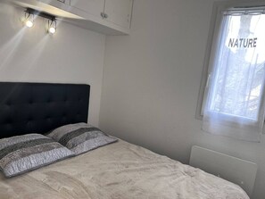 Ein Schlafzimmer mit einem Bett, zwei Nachttischlampen, einem Fenster mit Blick und einem Thermostat.
