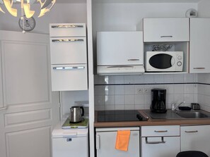 Eine kleine Küche mit weißen Schränken, einer Mikrowelle, einer Kaffeemaschine und einem Wasserkocher auf einer Waage.