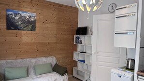 Ein Zimmer mit einer Holzwand, einem weißen Sofa mit grünen Kissen, einem weißen Bücherregal, einer weißen Tür und einem weißen Kühlschrank.