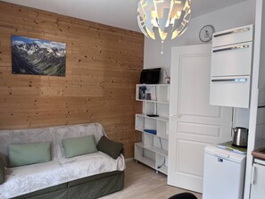 Ein Zimmer mit einer Holzwand, einem weißen Sofa mit grünen Kissen, einem weißen Bücherregal, einer weißen Tür und einem weißen Kühlschrank.