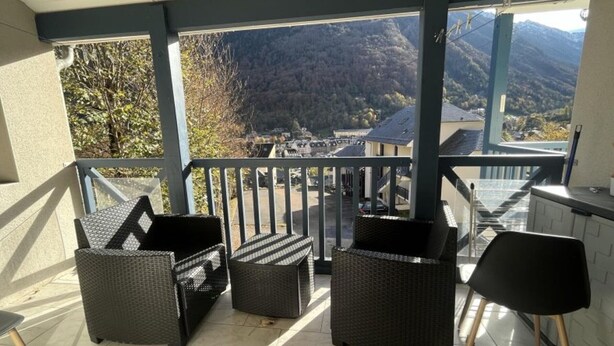 Ein Balkon mit Korbmöbeln, Blick auf eine Berglandschaft und einem Geländer.