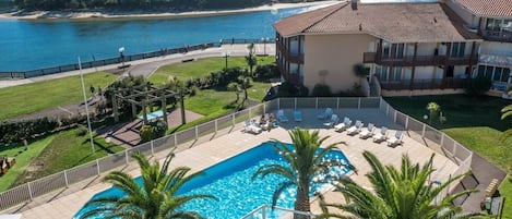 A resort with a large pool, palm trees, and a view of the sea.