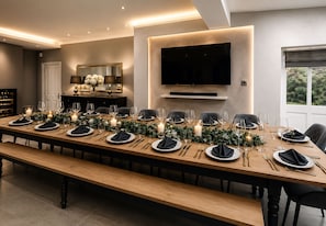 Una larga mesa de comedor dispuesta para una comida formal, con velas y follaje.