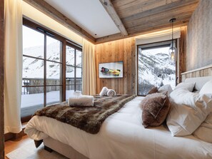A bedroom with a large bed, wooden walls, a window with a mountain view, and a mounted picture. - Apartment mountain view - 8 guests (Val-d'Isère)