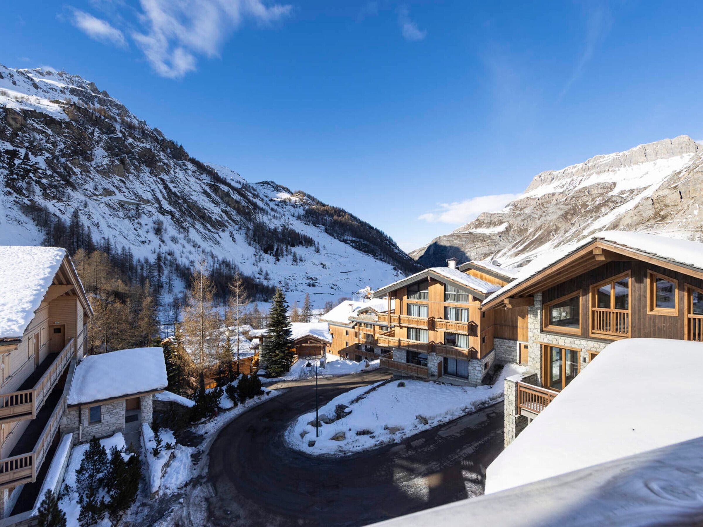 A mountain lodge with multiple wooden buildings, a snow-covered driveway, and a clear blue sky.