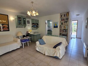 Ein Wohnzimmer mit einer Couch, einem kleinen Tisch mit Lampe, einer Küchenzeile mit Schränken und einem Bücherregal.