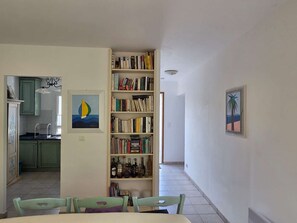 Ein Essbereich mit Tisch und Stühlen, ein Bücherregal mit Büchern und Flaschen sowie ein Gemälde an der Wand.