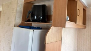 Een compacte keuken met een ingebouwde koffiezetapparaat, een witte koelkast en houten keukenkastjes.