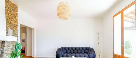Una sala de estar moderna con pared de piedra, un sofá tapizado oscuro, una lámpara colgante y vistas a través de una puerta de cristal.