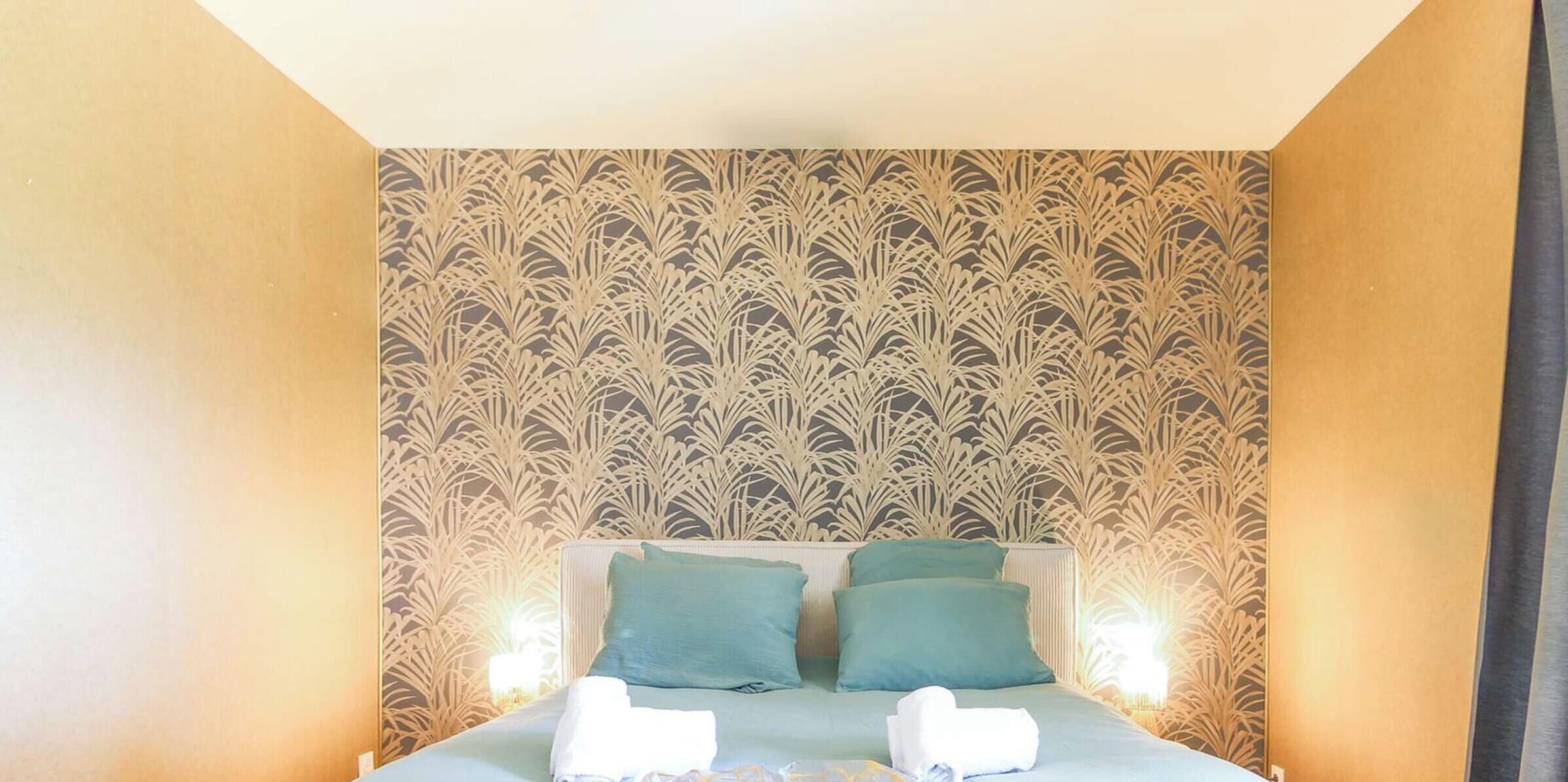 A hotel room with a patterned wallpaper, a bed with two pillows, and bedside lamps.