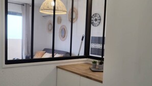 A room with a large window, a wooden shelf with potted plants, a white cabinet, and decorative wall art. - Renovated apartment, parking, AC, sea view - 4 guests (Canet-Plage)