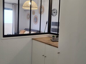A room with a large window, a wooden shelf with potted plants, a white cabinet, and decorative wall art. - Renovated apartment, parking, AC, sea view - 4 guests (Canet-Plage)