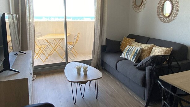 A living room with a sofa, a small table, and a balcony with a table and chairs. - Renovated apartment, parking, AC, sea view - 4 guests (Canet-Plage)
