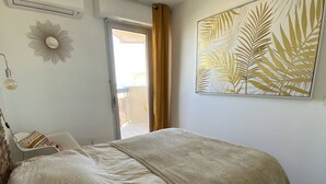 A bedroom with a bed, a chair, a window, and a door leading to a balcony. - Renovated apartment, parking, AC, sea view - 4 guests (Canet-Plage)