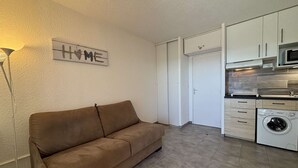 A compact living space with a sofa, a washing machine, and a kitchenette. - Studio cabin sea view - 3 guests (Cavalaire-sur-Mer)
