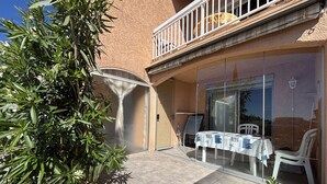 A patio area with a table and chairs, a glass door, and a balcony with a railing. - Studio cabin sea view - 3 guests (Cavalaire-sur-Mer)