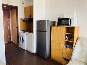 Eine kompakte Küche mit Waschmaschine, Kühlschrank, Mikrowelle und einem Holzkasten mit Schubladen.