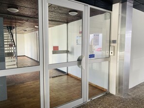 Ein moderner Aufzug mit Glastüren, einem gut sichtbaren Notausgangsschild und einer Metallhandläufe.