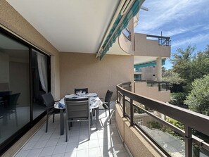Ein Balkon mit Tisch und Stühlen, eine Glastür und Blick auf ein Gebäude sowie Bäume.