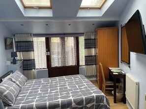 Una camera da letto con un letto, una scrivania, una sedia, un termosifone e un lucernario.