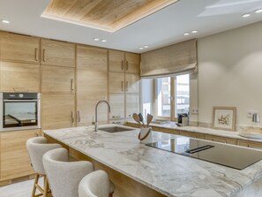 Eine moderne Küche mit Holzschränken, einer Marmorarbeitsplatte, einem eingebauten Backofen und einem großen Fenster.