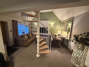 Una sala de estar con una escalera espiral, un sofá, una lámpara y un jarrón decorativo.